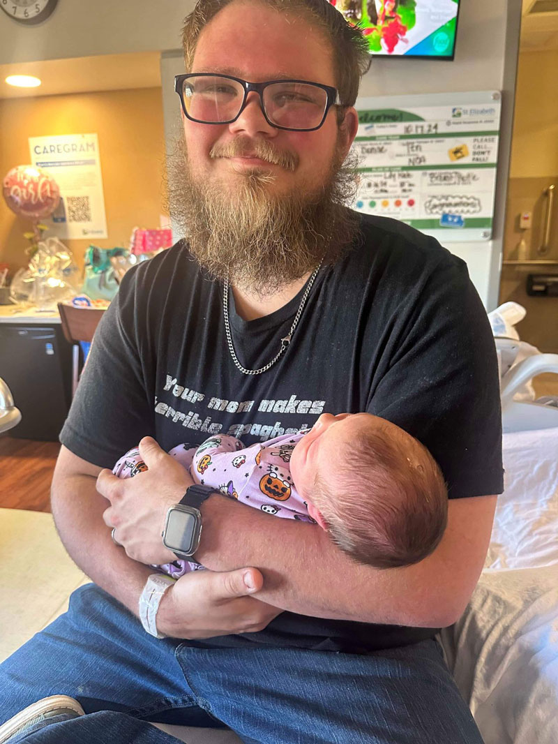 Skylar smiles at the camera while holding his newborn daughter LilyKate in his arms in the hospital.