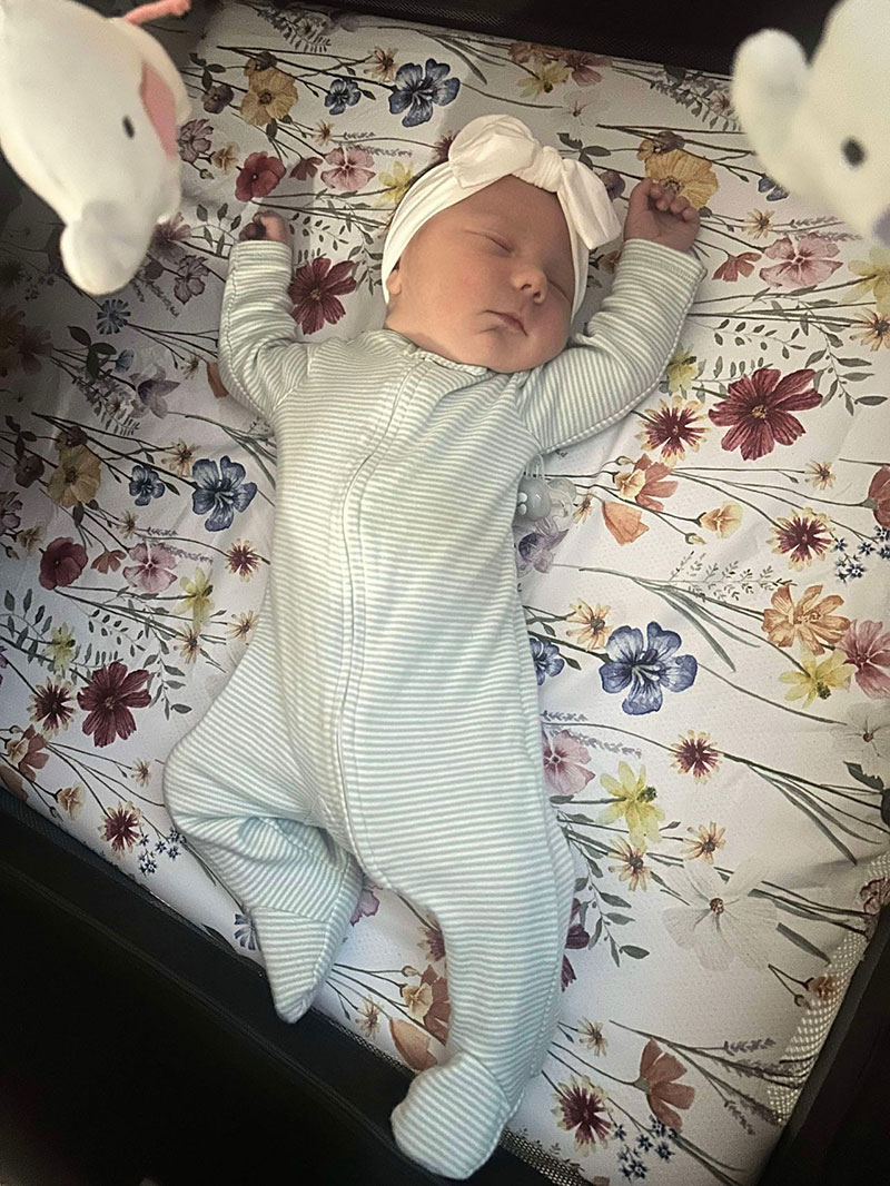 LilyKate is sprawled out in her crib taking a nap on her white floral sheets.